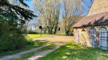 Un sentier rural menant à un bâtiment en pierre doté d’arches au niveau des fenêtres et d’un toit de chaume.