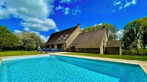 A swimming pool with clear blue water, surrounded by a grassy lawn and a stone building with a sloped roof. - Villa Choupinière - 30 pers-Pool-1h15 Paris (Choue)