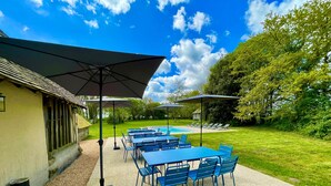 An outdoor patio with blue tables and chairs, umbrellas, and a pool in the background. - Villa Choupinière - 30 pers-Pool-1h15 Paris (Choue)