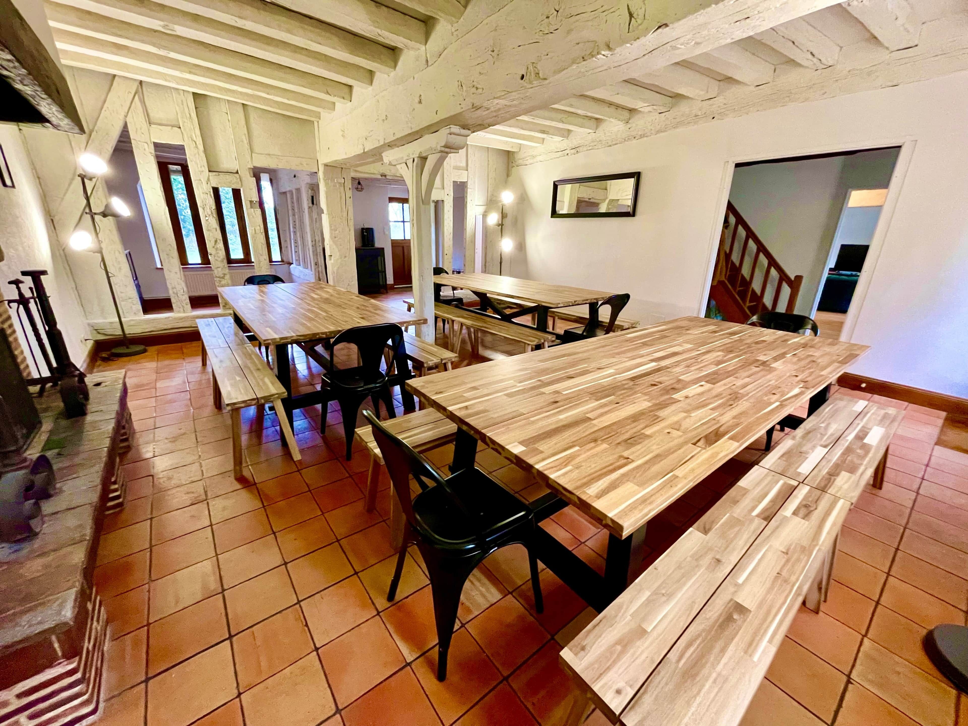 Uma área de refeições com mesas e bancos de madeira, piso de azulejos e escada que sobe.