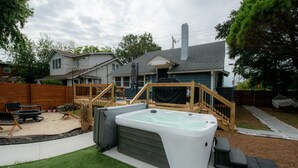 A backyard with a hot tub, wooden deck, and a house in the background. - Stylish Beach House, Hot Tub, Pet-Friendly🐾 (Norfolk)