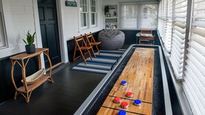 A room with a shuffleboard table, chairs, a bean bag, a small table with a plant, and a welcome sign. - Stylish Beach House, Hot Tub, Pet-Friendly🐾 (Norfolk)