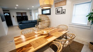 A dining area with a wooden table, wicker chairs, and a woven light fixture. - Stylish Beach House, Hot Tub, Pet-Friendly🐾 (Norfolk)