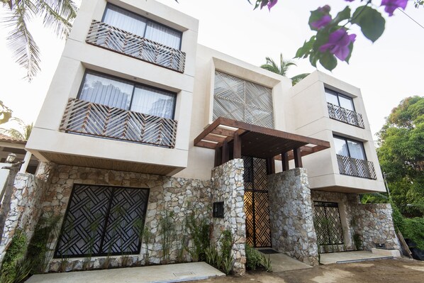 Un edificio moderno de dos pisos con fachada de piedra, diseños geométricos en las ventanas y un vestíbulo cubierto.