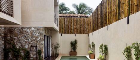 Una piscina con un muro de piedra y una cubierta de madera a un lado, y una valla de bambú al otro.