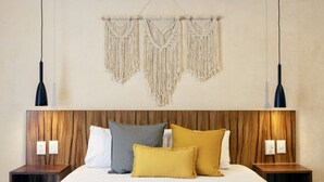 Ein ordentlich bezogenes Bett mit einem Holz-Kopfteil, mehreren Kissen und einem Wandbehang aus Makramee darüber.