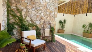 Eine Holzterrasse mit Steinmauer, einer Liege, einem kleinen Pool und Topfpflanzen.