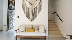 Ein Wohnzimmer mit einer Couch, einem Wandbehang aus Makramee, einer Treppe und einer Steinwand.