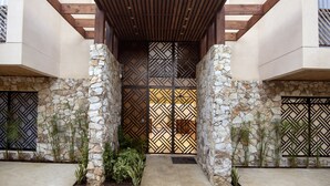Ein Gebäudeeingang mit einer Holzpergola, Steinmauern und verzierten Metallgittern.