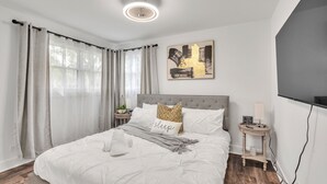 A modern bedroom with a bed, curtains, a bedside table, a lamp, and a wall art piece. - Modern Luxury Amenities Near Woodfield Mall 2 Bedroom Home by RedAwning (Rolling Meadows)