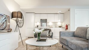 A modern living room with a grey sofa, a round coffee table with a vase of flowers, and a white cabinet. - Central Cambridge Studios - Tailored Stays (Cambridge)
