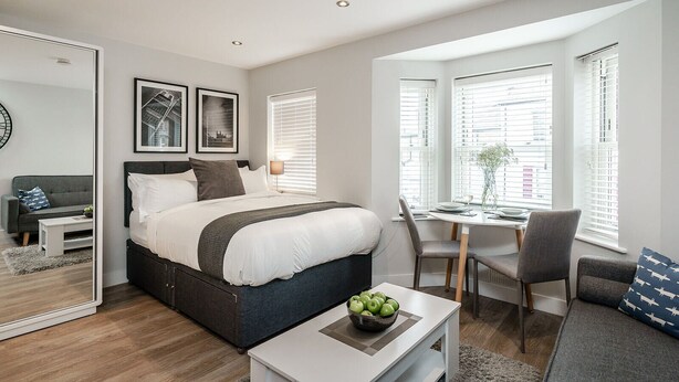 A modern bedroom with a large bed, a desk, and a dining area. - Central Cambridge Studios - Tailored Stays (Cambridge)