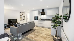 A modern living room with a grey sofa, a glass coffee table, and a TV. - Lacon House 2-bedroom apartment (Cambridge)