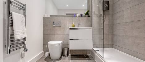 Un baño moderno con ducha de vidrio, inodoro blanco, lavamanos blanco y un perchero para toallas.