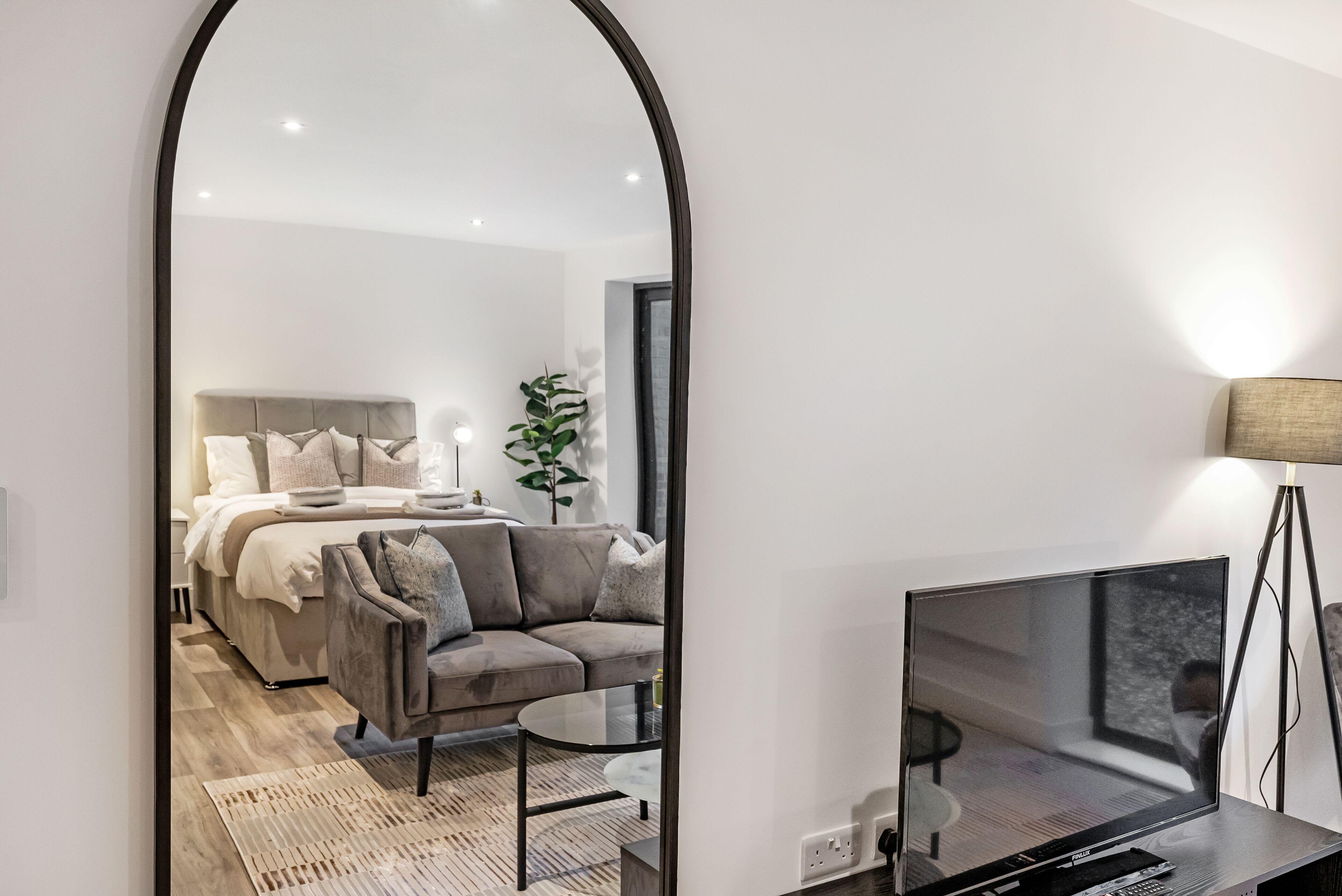Een moderne slaapkamer met een bed, een bank, een televisie en een spiegel.