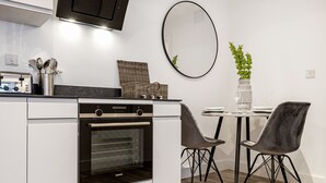 A modern kitchen with a built-in oven, a dining table with chairs, a hanging mirror, and a potted plant. - Lacon House 1-bedroom apartment (Cambridge)