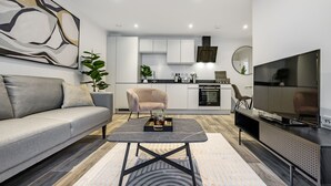 A modern living room with a grey sofa, a coffee table, and a TV on a stand. - Lacon House 1-bedroom apartment (Cambridge)