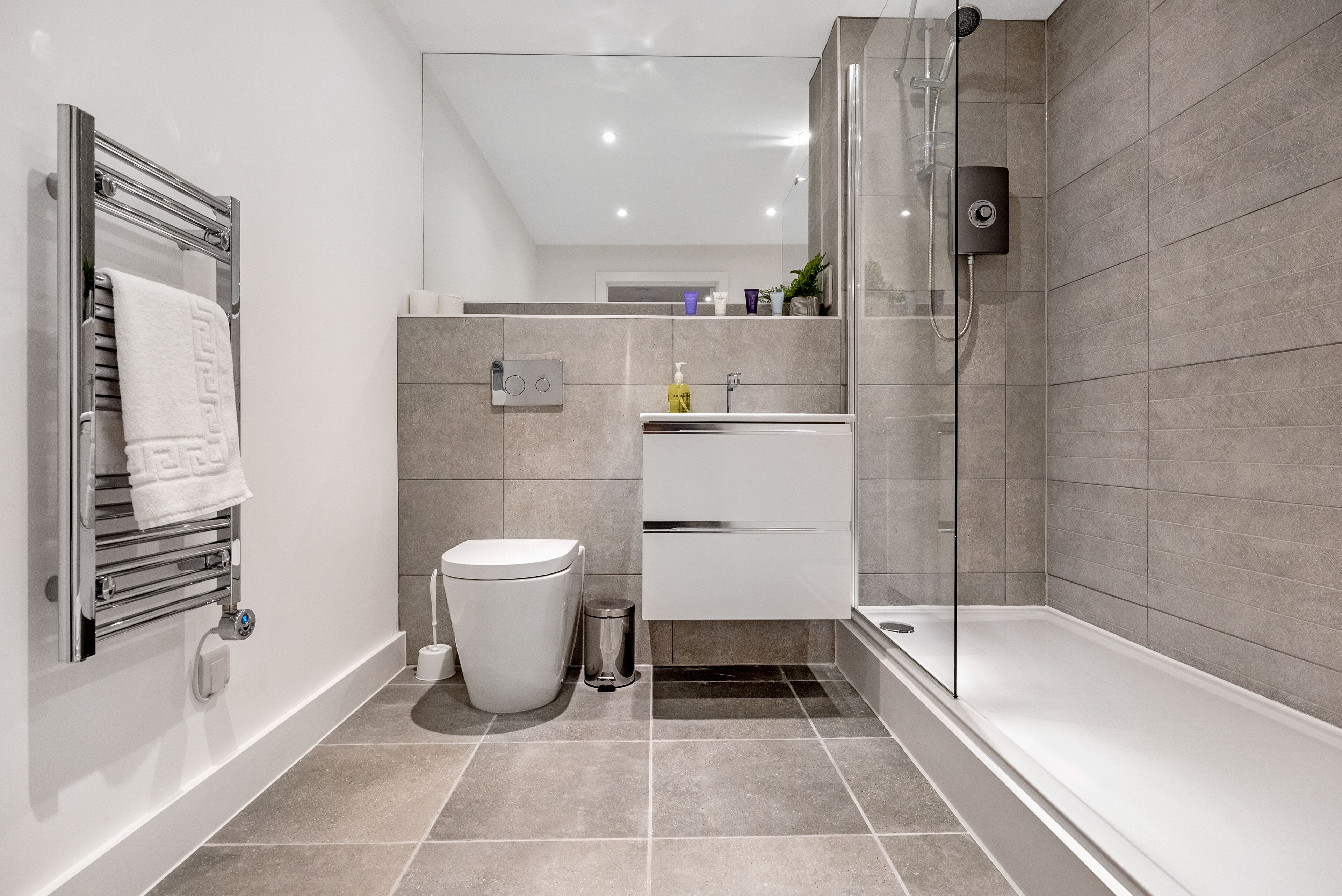 A modern bathroom with a glass-enclosed shower, a white toilet, a white sink, and a towel rack.