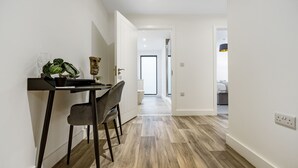 A modern kitchen with a dining area, featuring a wooden floor, white walls, and a view into the adjacent living room. - Lacon House 1-bedroom apartment (Cambridge)