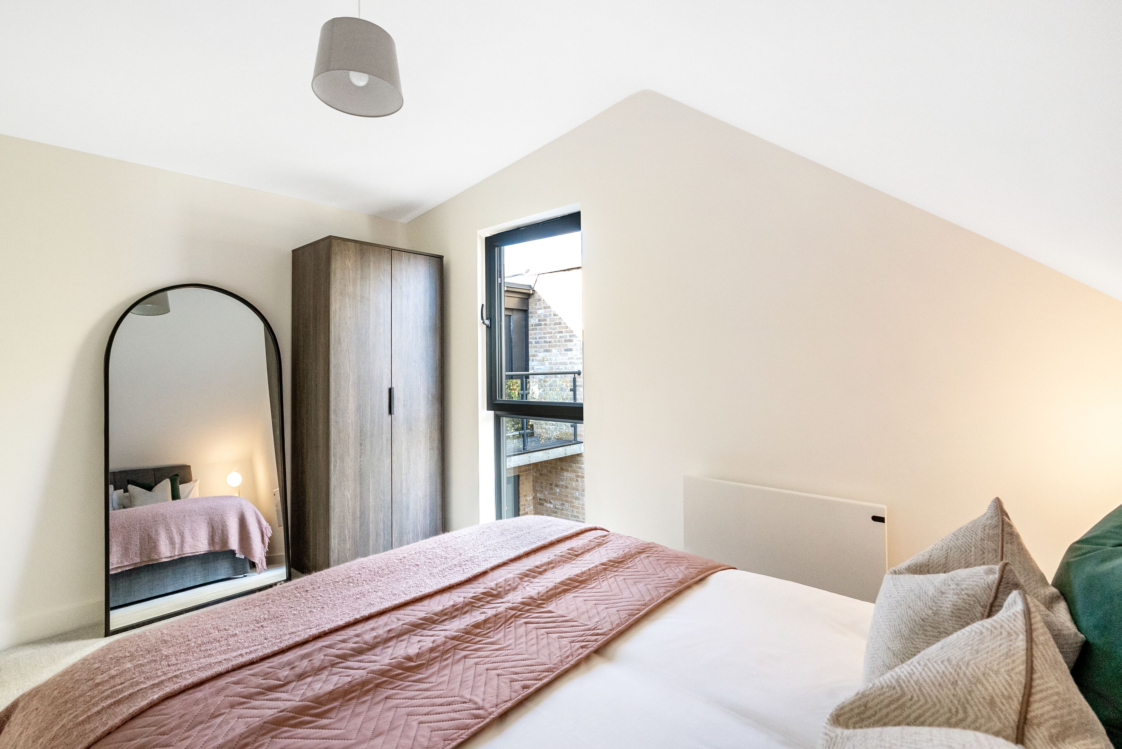 Un dormitorio con una cama, un espejo grande, un armario y una ventana que da a un edificio.