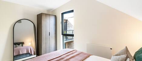 Un dormitorio con una cama, un espejo grande, un armario y una ventana que da a un edificio.