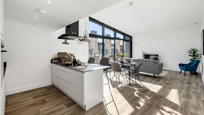 Eine moderne Küche mit Kochinsel, Essbereich mit Stühlen und Tisch sowie Wohnbereich mit Sofa und Fernseher.