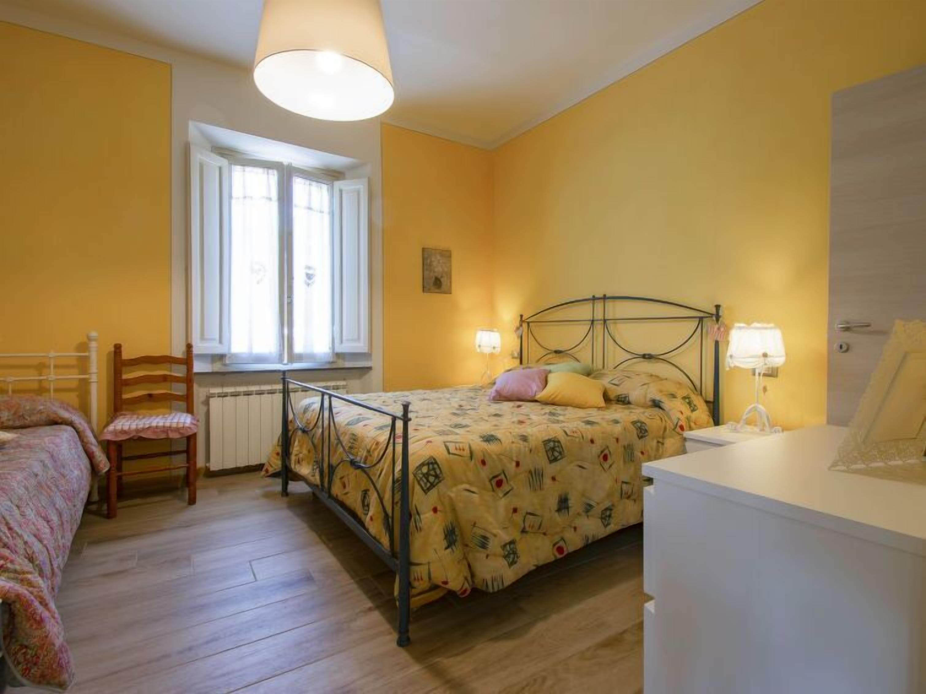 A bedroom with a bed, a chair, a window, and a bedside table with a lamp.
