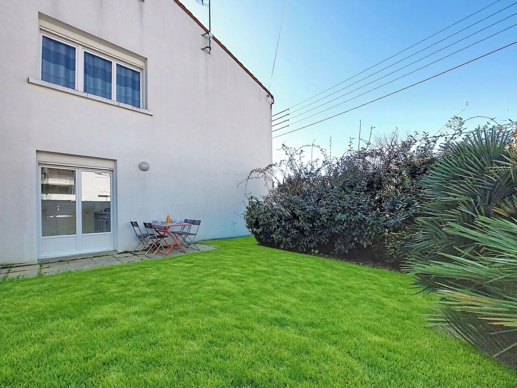 A residential property with a well-maintained lawn, a patio with outdoor furniture, and a hedge.