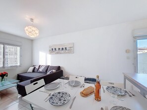 Una cocina moderna con encimeras blancas, una mesa de comedor preparada para cuatro personas y un amplio ventanal que proporciona luz natural.
