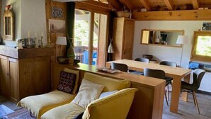 Ein gemütliches Blockhaus-Interieur mit einem Holzesstisch, zwei gelben Stühlen, einer Couch und einer Küchenzeile mit Holzschränken.