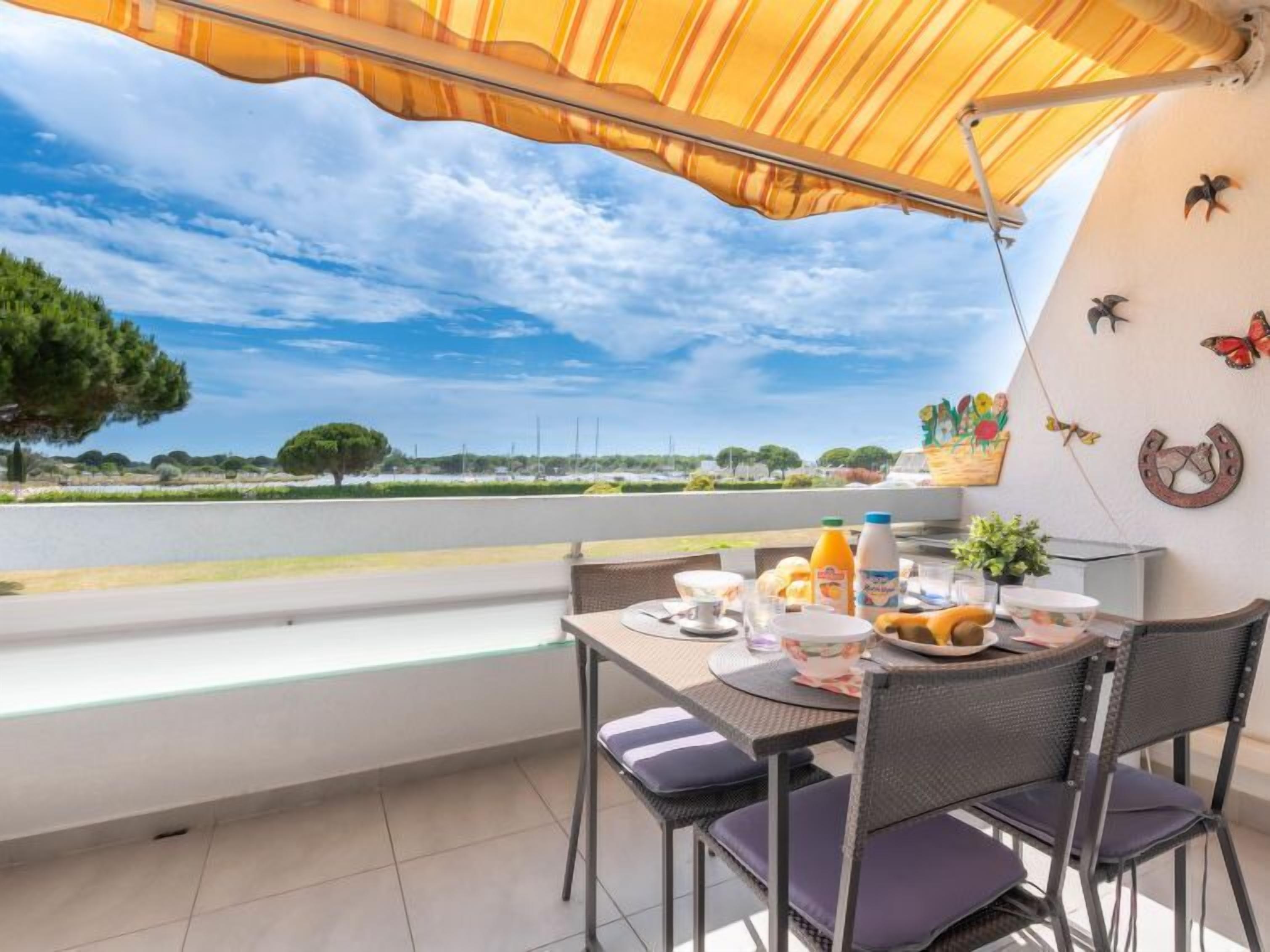 A balcony with a table set for breakfast, a view of the countryside, and decorative wall art.