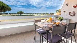A balcony with a table set for breakfast, a view of the countryside, and decorative wall art. - Isle Catherine by Interhome (Port Camargue)