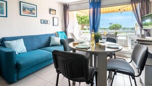 A living room with a blue sofa, a dining table with chairs, and a TV. - Isle Catherine by Interhome (Port Camargue)