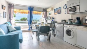 A compact living space with a sofa, dining table, chairs, a washing machine, and a kitchenette. - Isle Catherine by Interhome (Port Camargue)