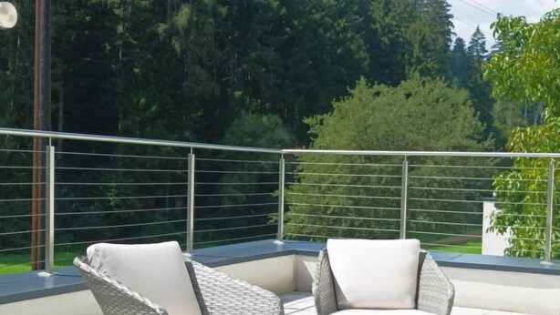 A balcony with two wicker chairs and a glass table, surrounded by a metal railing and greenery. - Apart Hof Achenrainer by Interhome (Landeck)