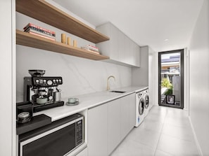 A modern kitchen with a coffee machine, a washing machine, and a sink. - Amila — Designer Coastal Retreat in Dunsborough (Dunsborough)