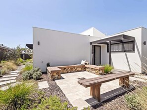 A modern outdoor patio area with a stone bench, a wooden table, and a covered seating area. - Amila — Designer Coastal Retreat in Dunsborough (Dunsborough)
