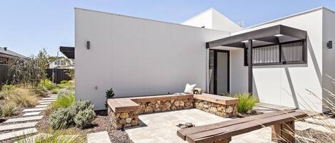 Un patio extérieur moderne doté d’un mur en pierre servant de banc, d’un banc en bois et d’une pergola offrant de l’ombre.
