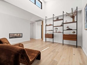 A modern living room with a brown sofa, wooden flooring, and a black metal shelving unit against the wall.