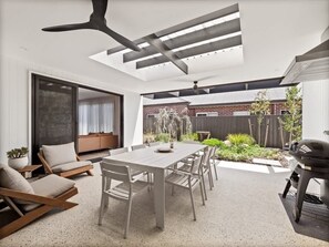 Un espace de vie ouvert comprenant un coin repas, un espace détente, un barbecue et une vue sur le jardin arrière.