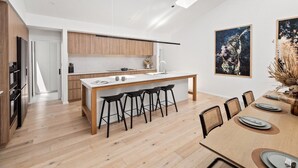 Moderni keittiö, jossa on kattoikkunat, ruokailutila puupöydällä ja -tuoleilla sekä taideteoksia seinillä.