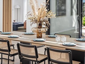 A dining area with a long table, black chairs, and a decorative vase with dried plants.