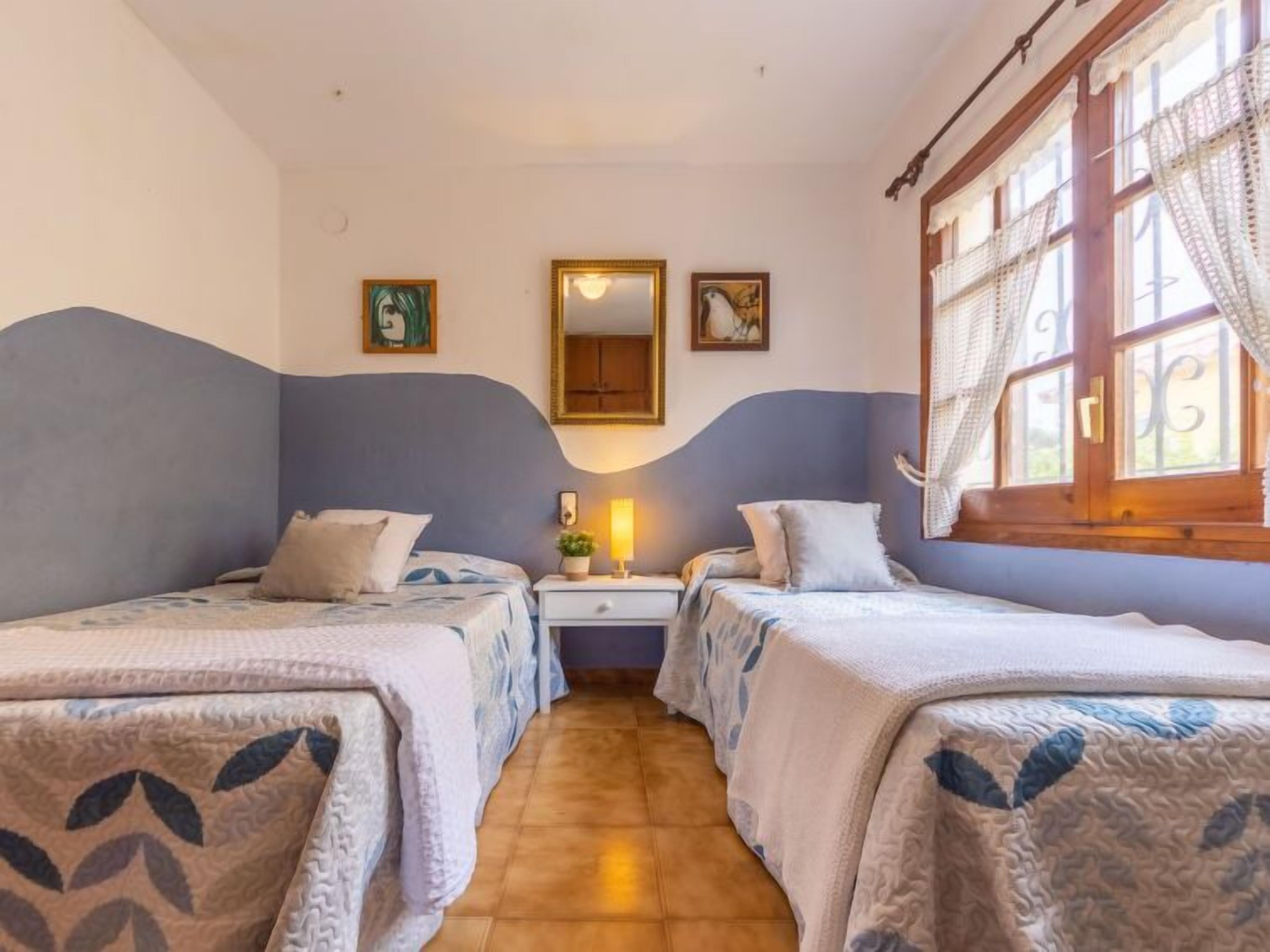 Una habitación con dos camas individuales, una mesita de noche con lámpara, un espejo y obras de arte en las paredes.