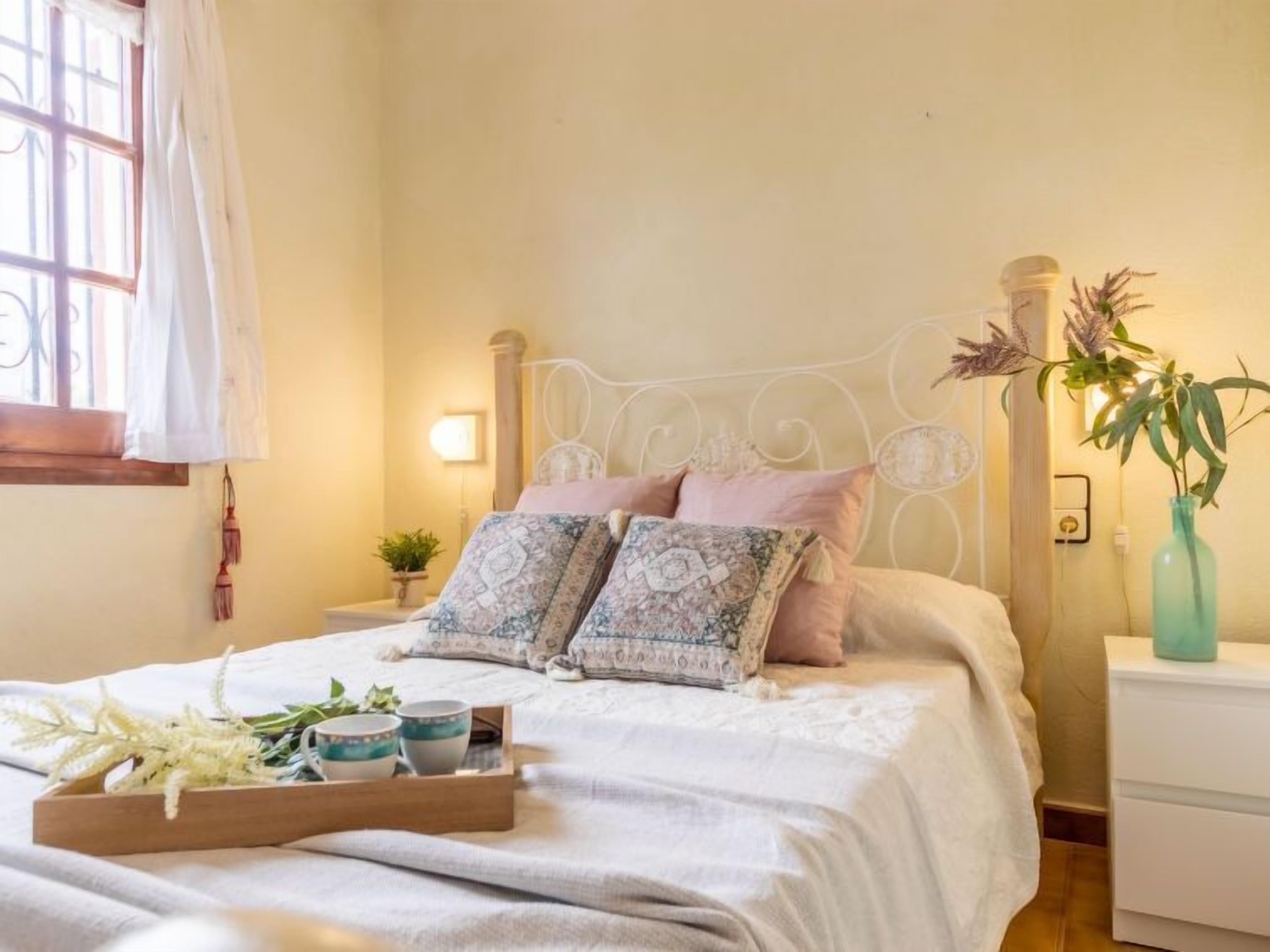A neatly made bed with patterned pillows, a bedside table with a lamp, and a window with curtains.