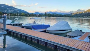 A wooden dock with boats, a clear lake, and mountains in the background.