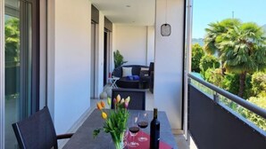 A balcony with a table set for two, a bottle of wine, and a vase of tulips.