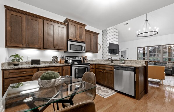 A modern kitchen with wooden cabinets, stainless steel appliances, and a glass dining table.