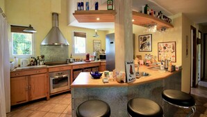 Une cuisine dotée de meubles en bois, d’une hotte de cuisinière en acier inoxydable, d’un four encastré, d’un coin café avec un panneau indicateur et d’une grande fenêtre avec des stores.