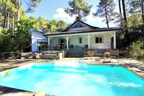 Ein Haus mit Swimmingpool, überdachter Terrasse und Blick auf den umliegenden Wald.