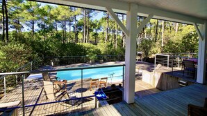 Un espace extérieur abrité avec une piscine, une terrasse en bois, des chaises longues et un coin barbecue.